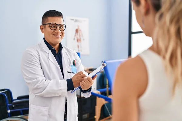 Young Latin Man Pysiotherapist Writing Report Speaking Patient Rehab Clinic — Stock Photo, Image