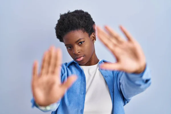 African american woman standing over blue background doing frame using hands palms and fingers, camera perspective