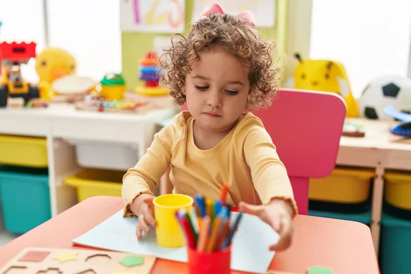 Adorable hispanic toddler student sitting on table drawing on paper at kindergarten