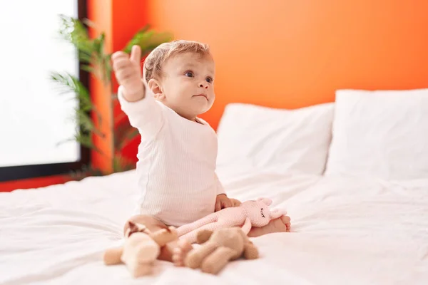 Sevimli Sarışın Bebek Elinde Oyuncak Bebekle Yatakta Oturuyor — Stok fotoğraf
