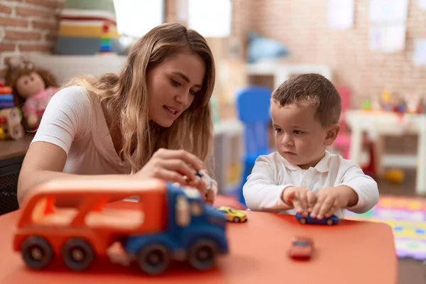 Teacher and toddler playing with cars toy sitting on table at kindergarten