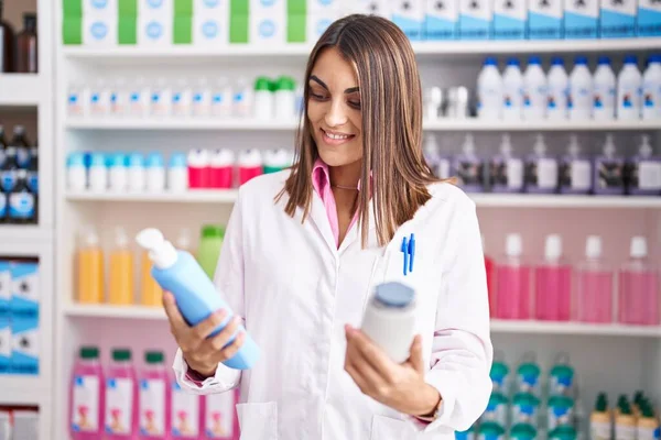 Young Beautiful Hispanic Woman Pharmacist Holding Shampoo Bottles Pharmacy — Foto Stock