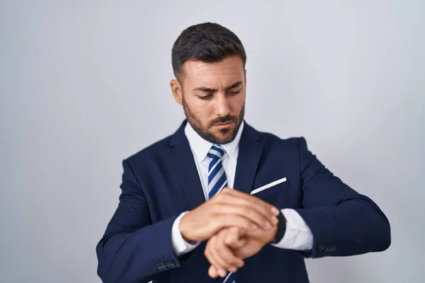 Handsome hispanic man wearing suit and tie checking the time on wrist watch, relaxed and confident