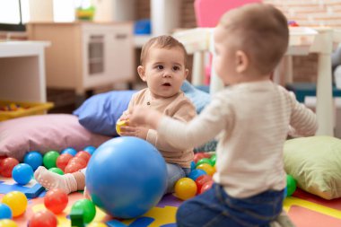 Anaokulunda yerde oturmuş hayalarıyla oynayan iki sevimli çocuk.