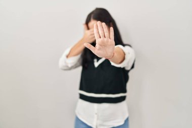 Soyutlanmış arka planda duran genç İspanyol kadın elleriyle gözlerini kapatıyor ve üzgün ve korku ifadesiyle dur hareketi yapıyor. utangaç ve olumsuz kavram. 