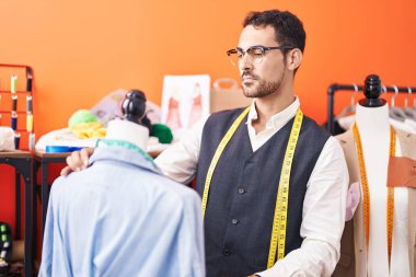 Young hispanic man tailor measuring shirt at atelier