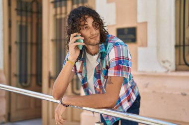 Young hispanic man talking on smartphone with serious expression at street