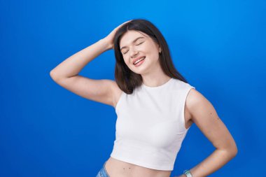 Young caucasian woman standing over blue background smiling confident touching hair with hand up gesture, posing attractive and fashionable 