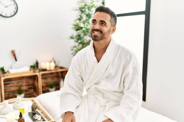 Güzellik merkezinde kendine güvenen genç İspanyol bir adam bornoz giyiyor.