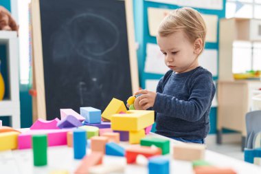 Anaokulundaki masada oturan sevimli sarışın çocuk geometri bloklarıyla oynuyor.