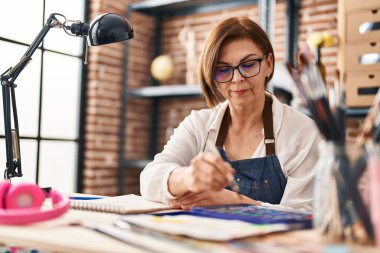 Middle age woman artist drawing on notebook at art studio