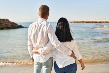 Kadın ve erkek deniz kenarında birbirlerine sarılıyorlar.