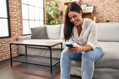 Evdeki kanepede oturan akıllı telefon kullanan genç, güzel İspanyol kadın.