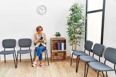 Orta yaşlı, sarışın, kendine güvenen, bekleme odasında müzik dinleyen bir kadın.