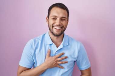 Hispanic man standing over pink background smiling and laughing hard out loud because funny crazy joke with hands on body. 