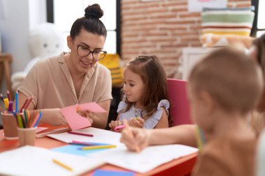 Teachers with boy and girl smiling confident cutting paper at kindergarten