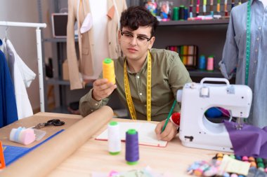 Non binary man tailor writing on notebook holding thread at atelier