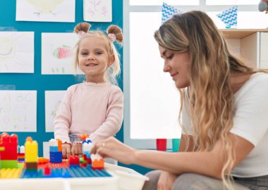 Teacher and toddler playing with construction blocks sitting on table at kindergarten