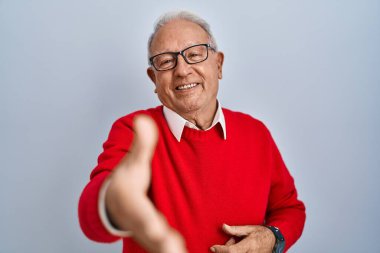 Senior man with grey hair standing over isolated background smiling friendly offering handshake as greeting and welcoming. successful business. 