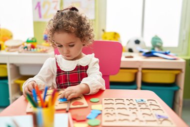 Adorable hispanic toddler playing with maths puzzle game sitting on table at kindergarten