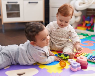 Anaokulunda yerde oturmuş oyuncaklarla oynayan iki sevimli bebek.