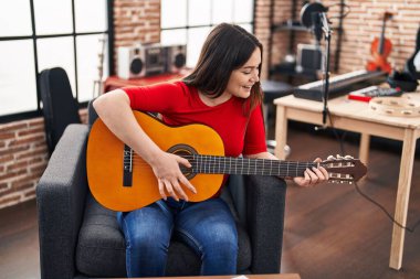 Young woman musician playing classical guitar at music studio