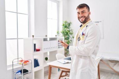 Young hispanic man wearing doctor uniform standing at clinic