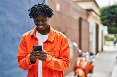 Sokakta akıllı telefon kullanan, kendinden emin gülümseyen Afrikalı Amerikalı bir adam.