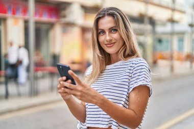 Sokakta akıllı telefon kullanan, kendine güvenen genç sarışın kadın.