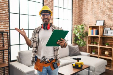 Sakallı genç İspanyol bir adam ev tadilatında çalışıyor başarıyı mutlu bir gülümsemeyle kutluyor ve kazanan el kaldırarak ifade ediyor. 