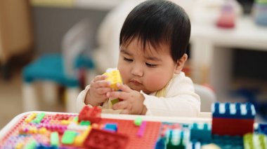 Adorable hispanic baby playing with construction blocks sitting on table at kindergarten
