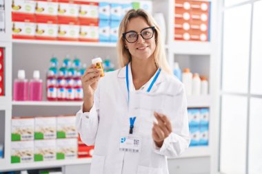 Genç sarışın eczacı elinde ilaç şişesiyle eczanede reçete okuyor.