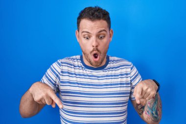 Mavi arka planda dikilen genç İspanyol adam parmaklarını göstererek reklamını yapıyor, şaşırmış yüz ve ağzını açıyor. 