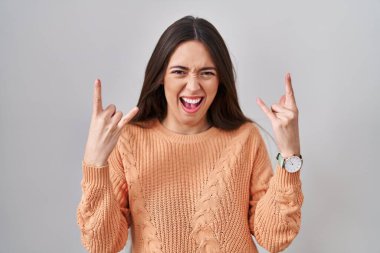 Young brunette woman standing over white background shouting with crazy expression doing rock symbol with hands up. music star. heavy music concept. 