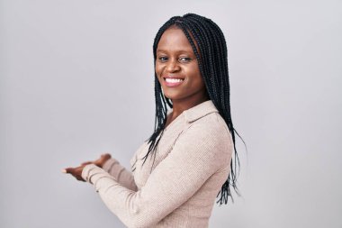 African woman with braids standing over white background inviting to enter smiling natural with open hand 