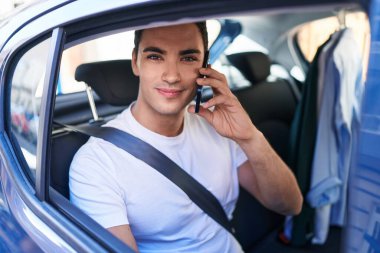 Genç İspanyol adam akıllı telefondan konuşuyor. Sokakta arabada oturuyor.