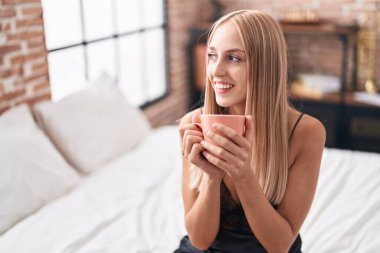 Genç sarışın kadın yatakta bir fincan kahve içiyor.