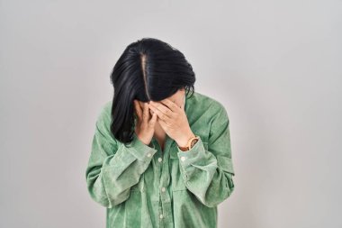 Young asian woman standing over white background with sad expression covering face with hands while crying. depression concept. 