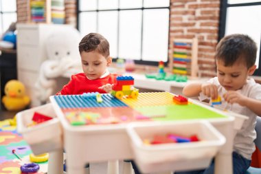 Two kids playing with construction blocks sitting on table at kindergarten