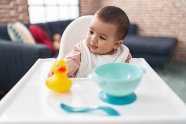 Adorable hispanic baby smiling confident sitting on highchair at home
