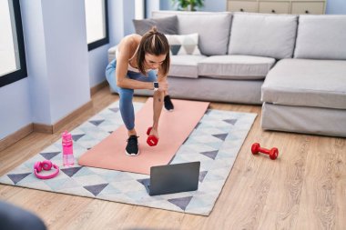 Young beautiful hispanic woman having online training with dumbbells at home