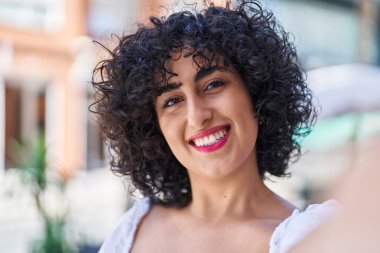 Orta Doğulu genç bir kadın gülümsüyor. Sokakta kameranın önünde özçekim yapıyor.