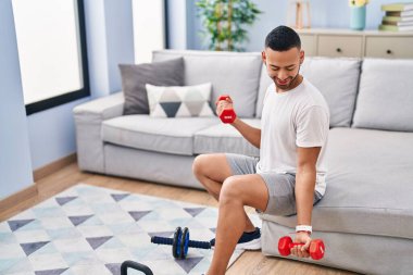 African american man smiling confident using dumbbells training at home