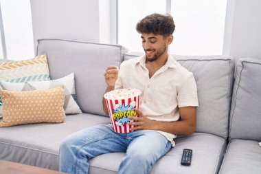 Young arab man eating popcorn watching movie at home