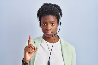 African american woman wearing call center agent headset pointing up looking sad and upset, indicating direction with fingers, unhappy and depressed. 
