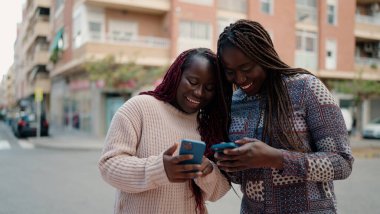 Two african american friends smiling confident using smartphone at street
