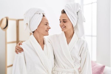 Two women mother and daughter wearing bathrobe hugging each other at bedroom