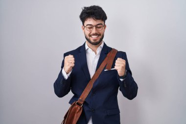 Hispanic man with beard wearing business clothes excited for success with arms raised and eyes closed celebrating victory smiling. winner concept. 