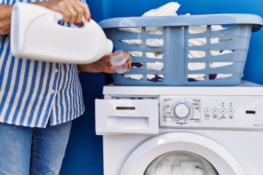 Yaşlı gri saçlı kadın gülümsüyor çamaşırhanedeki çamaşır makinesine deterjan döküyor.