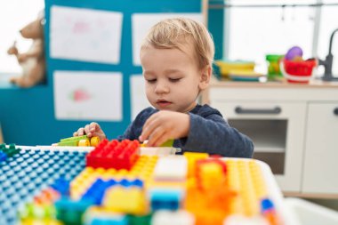 Anaokulundaki masada oturan sevimli sarışın çocuk inşaat bloklarıyla oynuyor.